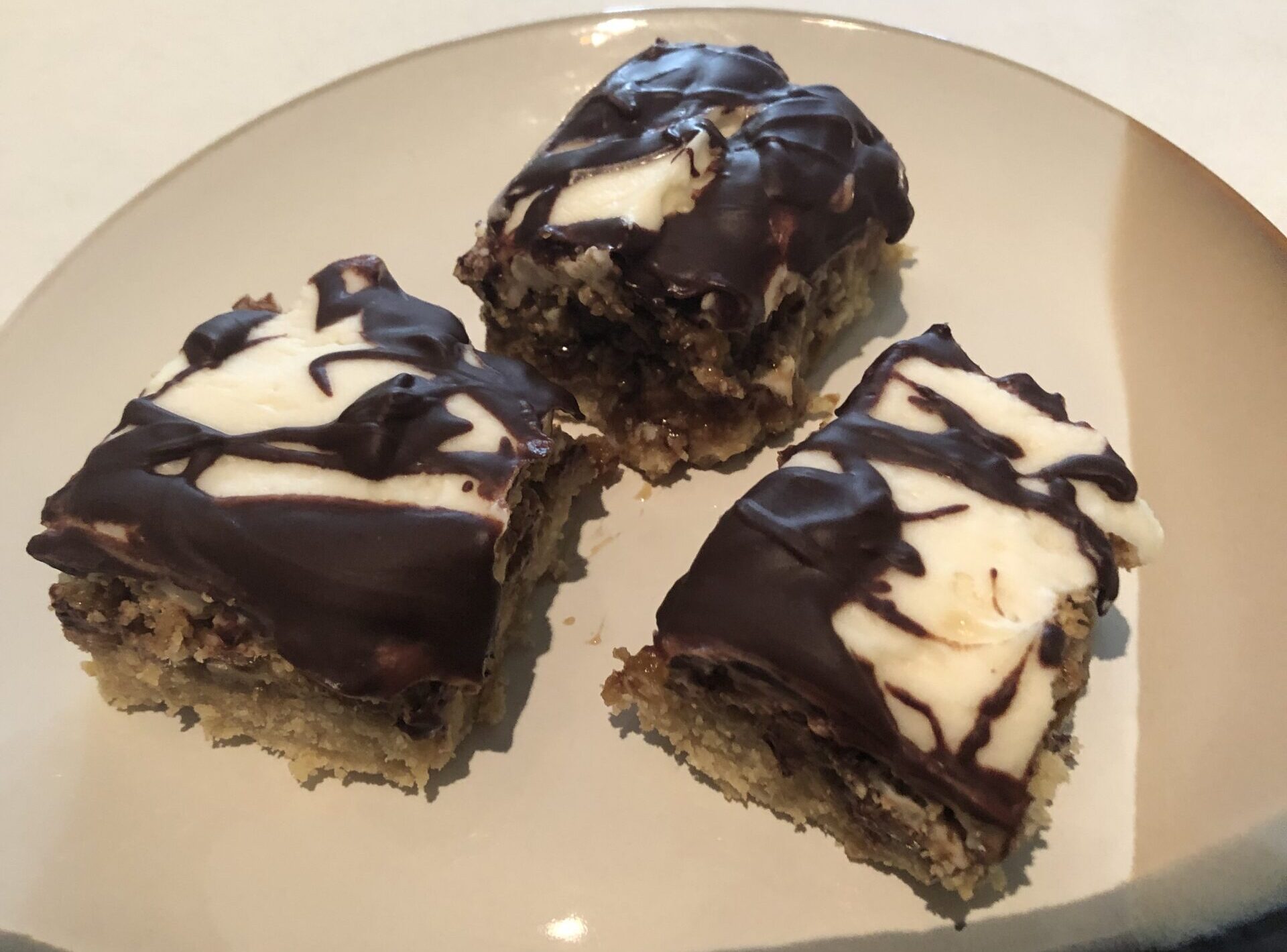 Three dessert bars with white frosting and a chocolate drizzle.