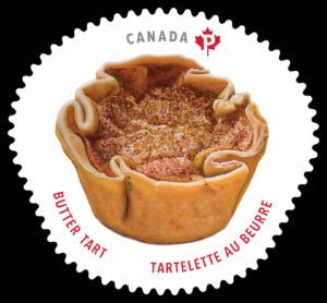 A Canadian postage stamp with a butter tart image. It is rounded, to adhere to the shape of the tart and has a scalloped edge. The top reads "CANADA" with a maple leaf containing the letter "P". The bottom reads "Butter Tart Tartelette Au Beurre"