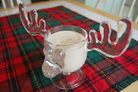 A creamy beverage with nutmeg sprinkled on top in a glass shaped like a moose head on a piece a red and green tartan fabric.